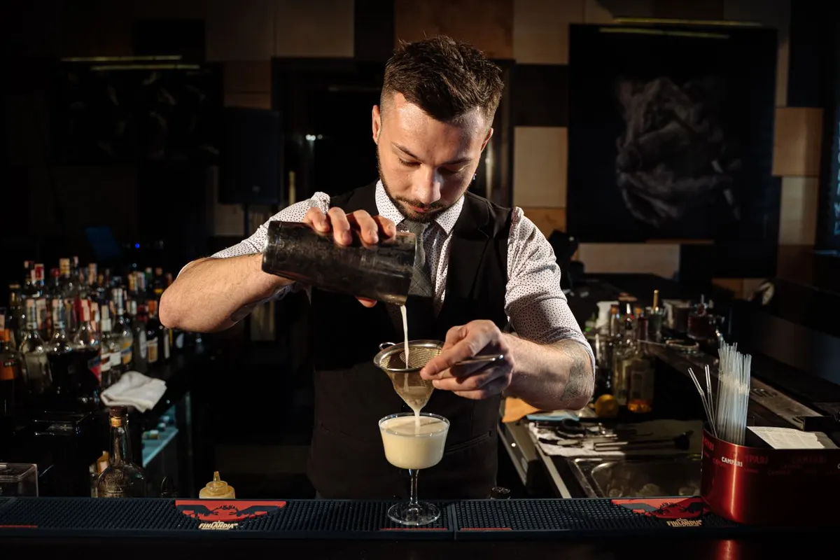 Bartender con chaleco preparando un cóctel de autor